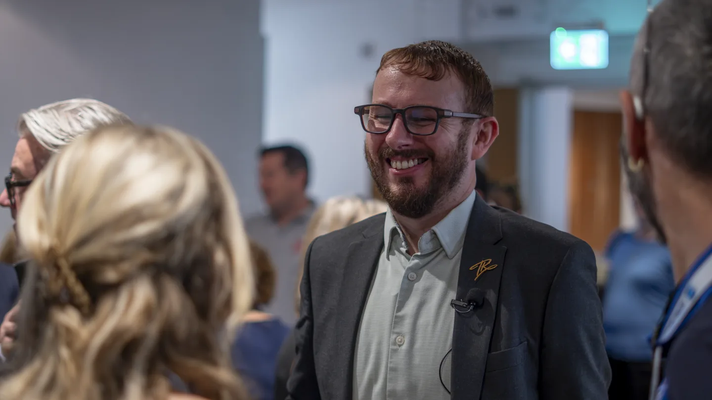 Tom Reveley smiling as he speaks with an attendee at Synergy Summit 2026