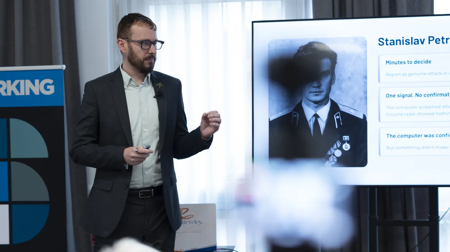 Tom Reveley speaking beside a screen displaying Stanislav Petrov at Synergy Summit 2026
